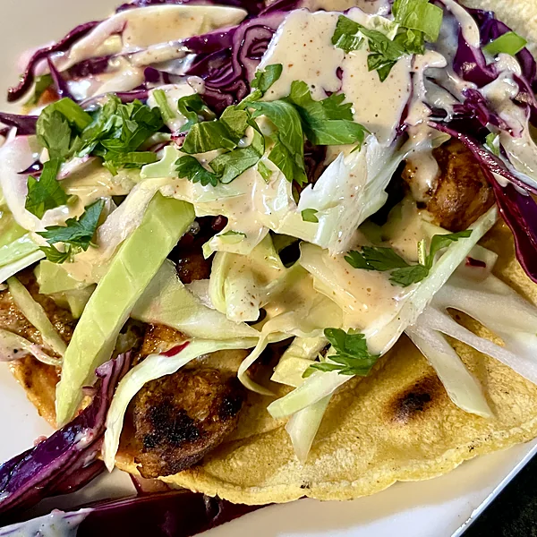 Corn tortilla tacos topped with red and green cabbage slaw, cilantro and creamy sauce