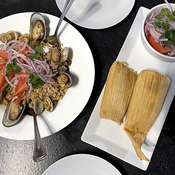 Seafood rice with mussels and clams beside two humitas in corn husks and a tomato onion salad