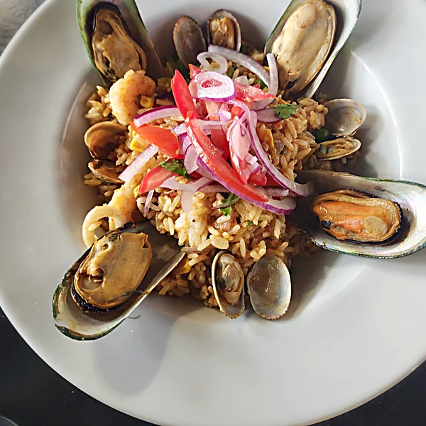 Seafood rice with mussels, clams, shrimp, tomato and red onion in a white bowl